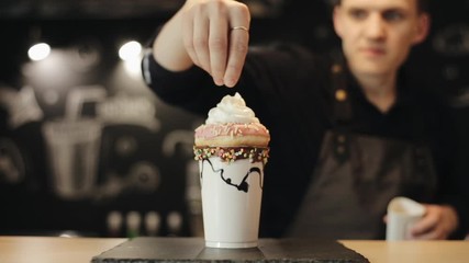 A male barista hand sprinkling confectionary dressing over milkshake with donut and whipped cream - Powered by Adobe