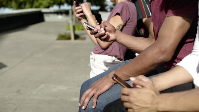 Side view of people using digital devices on street. Friends sitting in row with smartphones. Technology concept