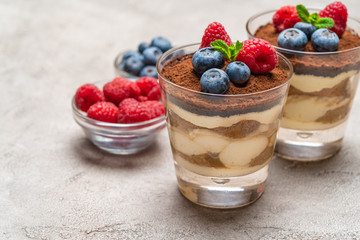 Classic tiramisu dessert with blueberries and raspberries in a glass and bowls with berries on concrete background