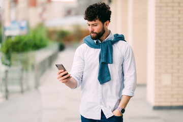 Young casual man using a smart phone texting messages in the street
