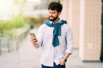 Happy guy having walk in the city and typing sms in the street