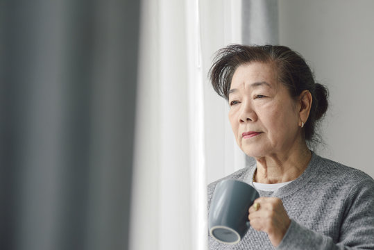 Asian senior woman drinking hot tea near window outdoor, lonely concept.