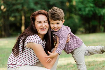 Happy mother with cute little boy having fun outdoors. Cheerful woman playing with her son in park. Joyful motherhood.