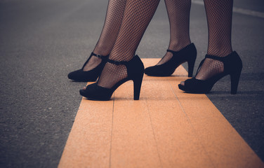 Two elegant woman wearing high heeled black shoes and sexy fishnet stockings modelling on wooden boards with foreground copy space in a low angle on their legs