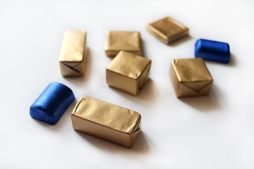 Chocolate candies wrapped in blue and golden foil isolated on white surface. Template for greeting card, poster or invitation. Sweets scattered on white smooth table. Backdrop or background