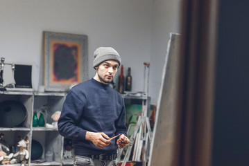 Portrait of an artist student with a brush in his hand in a cozy art studio near an easel with a canvas. Man studies painting in an art studio. Learning painting.