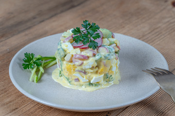 Delicious salad with cucumber, radish and egg with cream sauce in a plate on wooden background. Healthy food, close up