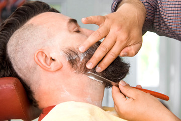 Barbershop. Master makes out a beard to a man with a mohawk.