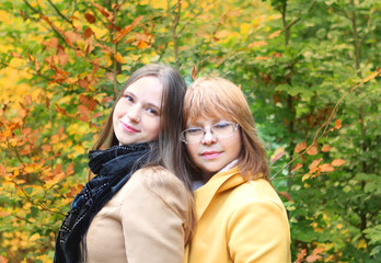 two people, mother and daughter, a woman and a young girl hold hands, clung to each other in a yellow autumn park, throw fallen leaves, the concept of family relationships, generations, close-up