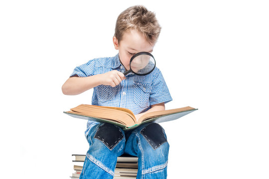 A pretty boy with a magnifying glass is reading a book on a white background. Isolated.
