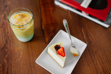 A piece of delicious cake with strawberry on top. Cold frappe beside.