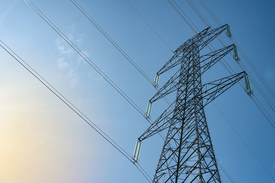 Overhead electrical power lines on a transmission tower against blue sky background. Electric energy distribution concept.