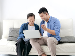 asian man teaching his mother using laptop at home, technology concept.