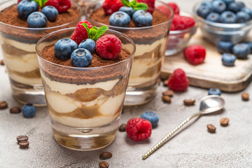 Classic tiramisu dessert with blueberries and raspberries in a glass and bowls with berries on concrete background