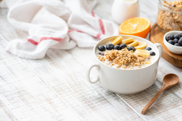 Granola with blueberry, banana and milk in white bowl on wooden table. Clean eating, healthy...