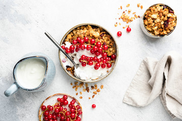 Oat granola with natural yogurt and red currant berries in bowl. On grey concrete background. Table top view. Healthy breakfast food, clean eating dieting weight loss concept