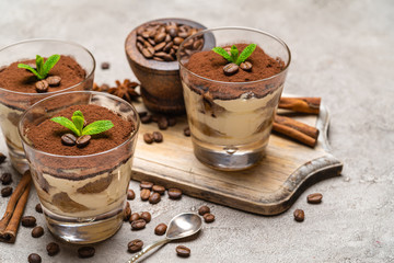 Classic tiramisu dessert in a glass and cinnamon sticks on concrete background
