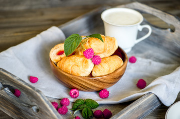 Croissants with raspberries on a wooden tray. The concept of a wholesome breakfast.
