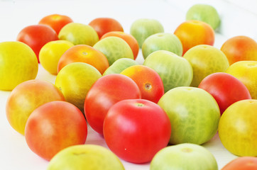 Red, green and yellow tomatoes on white background. Tomatoes of different colors and varieties. Juicy tomatoes on a white table. Colorful vegetables.