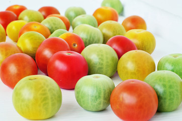 Red, green and yellow tomatoes on white background. Tomatoes of different colors and varieties. Juicy tomatoes on a white table. Colorful vegetables.
