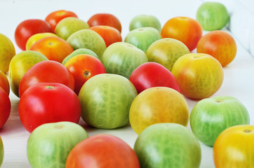 Red, green and yellow tomatoes on white background. Tomatoes of different colors and varieties. Juicy tomatoes on a white table. Colorful vegetables.