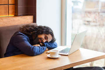 Tired handsome young adult man freelancer in casual style sitting in cafe with laptop, sleeping on the table after hard overtime work, closed eyes, bussinessman in office. Indoor, lifestyle concept