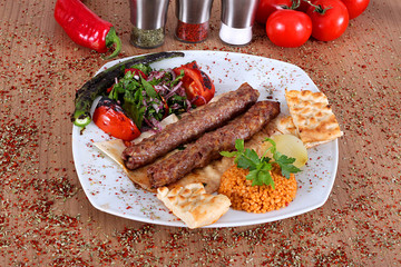 Roasted turkey and tomato kebabs with fresh pepper bread and vegetables on a wooden table filled with Turkish spices