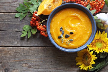 Pumpkin cream soup served on rustic wooden table with ingredients and festive autumn decoration....