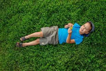 A little boy  lies on the green grass and dreams of something.  Happy childhood