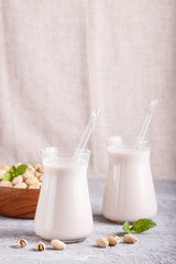 Organic non dairy pistachio milk in glass and wooden plate with pistachio nuts on a gray concrete background.