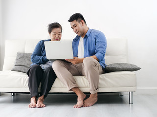 Asian man teaching his mother using laptop at home, technology concept.