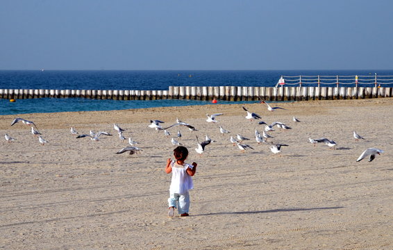 A happy baby girl running chasing the seagles at the beach with white sand in Dubai, UAE