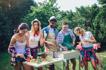 Young friends having fun grilling meat enjoying barbecue party.