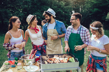 Young friends having fun grilling meat enjoying barbecue party.