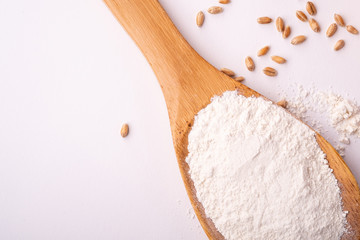 Wheat flour in wooden spoon spatula near with heap of grains, top view, flat lay, isolated on white background, copy space