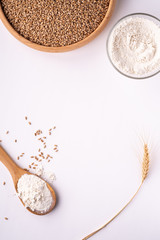 Wheat seeds grains in wooden bowl, wheat flour in glass bowl, near with flour in spoon spatula with heap of grains and with ear of wheat, top view, flat lay, isolated on white background, copy space