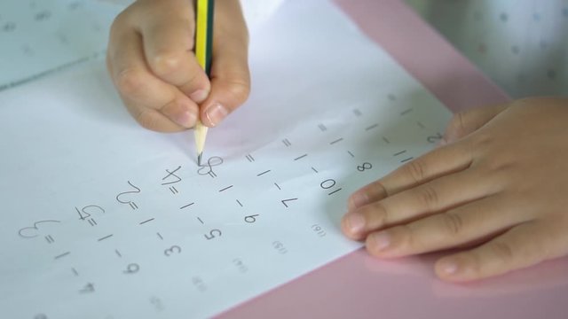hand of child or student holding pencil and study with learning writing number and practice minus mathematics on paper book or homework in home or classroom at school or kindergarten and nursery slow