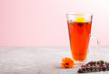 Glass of herbal tea with calendula and hyssop on a gray and pink background. Side view, copy space.
