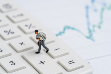 Miniature people figurine businessman walking on calculator from minus to plus button with graph and chart using as stock go up, rising or business performance success, profit and loss in accounting