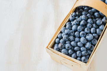 Fresh organic blueberries in a basket on white wooden background.