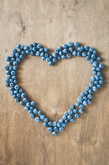 Fresh organic blueberries in form of heart on wooden background.