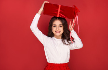 Fototapeta na wymiar pretty beautiful young litle girl celebration happy holidays merry Christmas Eve New Year party hold gift box present surprise isolated St. Valentine's Day on red background sale 