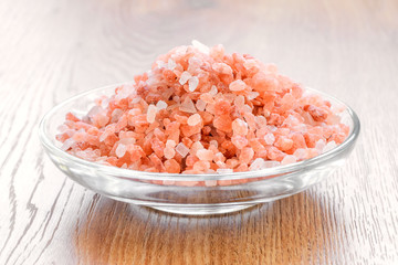 Fototapeta na wymiar Large crystals of pink himalayan salt in a glass saucer on a wooden table. Himalayan salt is used in cooking, medicine and cosmetology.