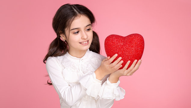 Close-up portrait of smiling little girl she nice-looking attractive lovely cute charming sweet cheerful  holding in hands  big red heart  isolated over pink pastel background