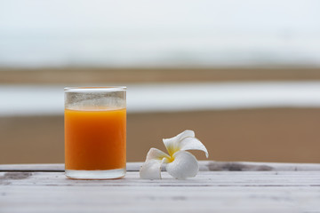 A glass of orange juice and plumeria alba on wooden table