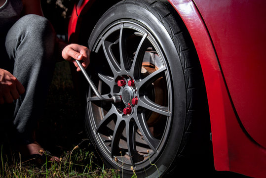 Man Hand With Wrench Tightens A Beautiful Car Wheel Towards A Red Car