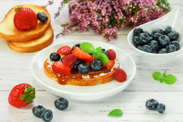 Delicious breakfast. Delicacy sandwich Toasts with cream cheese or mascarpone, caramel (iris toffee) and fresh berries - blueberries, raspberries, strawberries, peach  and mint. Selective focus