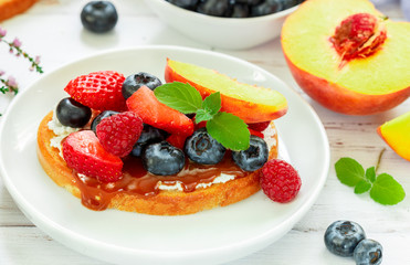 Delicious breakfast. Delicacy sandwich Toasts with cream cheese or mascarpone, caramel (iris toffee) and fresh berries - blueberries, raspberries, strawberries, peach  and mint. Selective focus