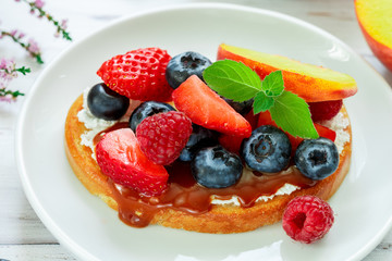 Delicious breakfast. Delicacy sandwich Toasts with cream cheese or mascarpone, caramel (iris toffee) and fresh berries - blueberries, raspberries, strawberries, peach  and mint. Selective focus