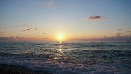 Beautiful sunset on Pebble beach and sea. Waves attack the stony beach.
